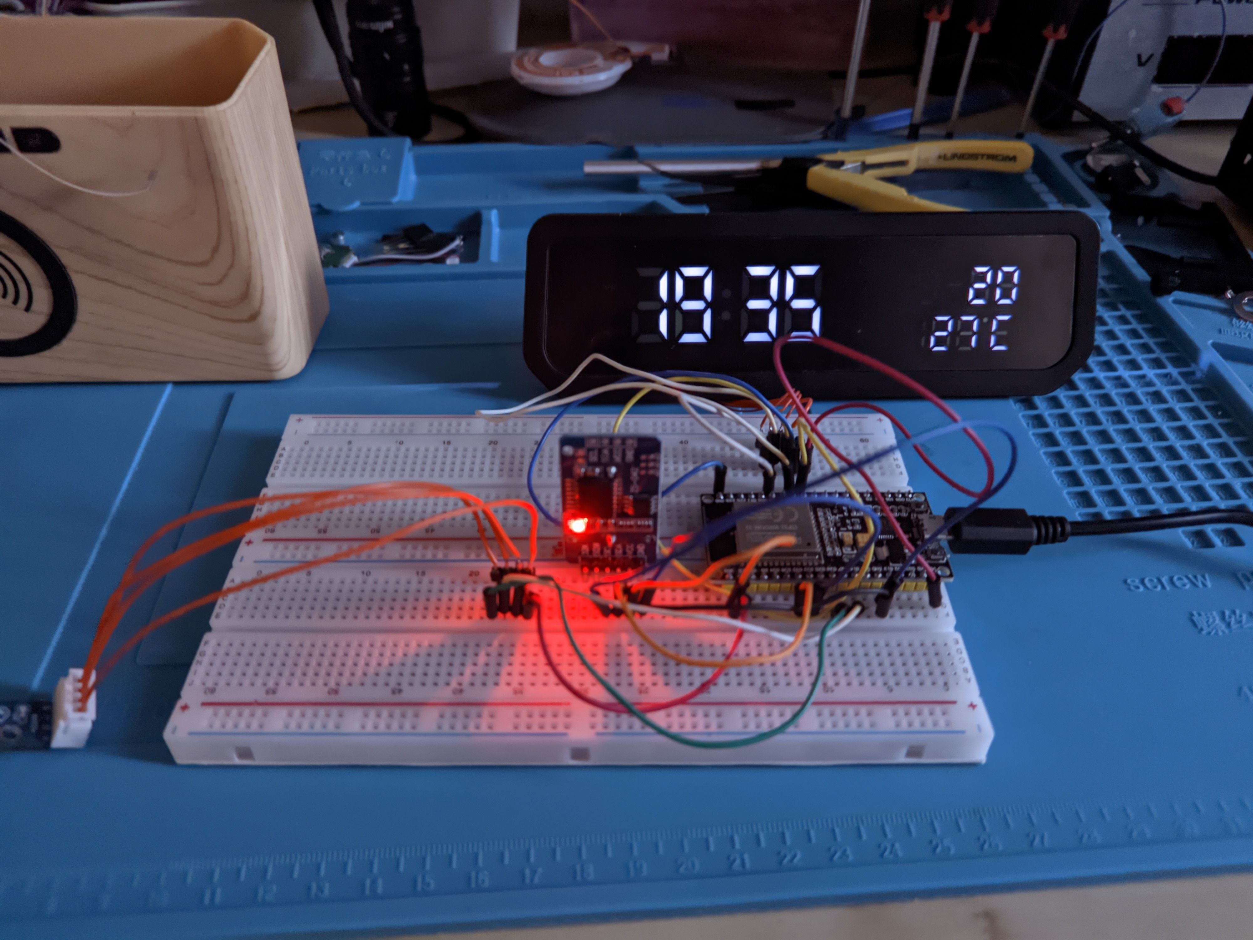 A black clock display with white 7-segment LEDs showing 19:35 and 27°C summer temperatures next to a breadboard.